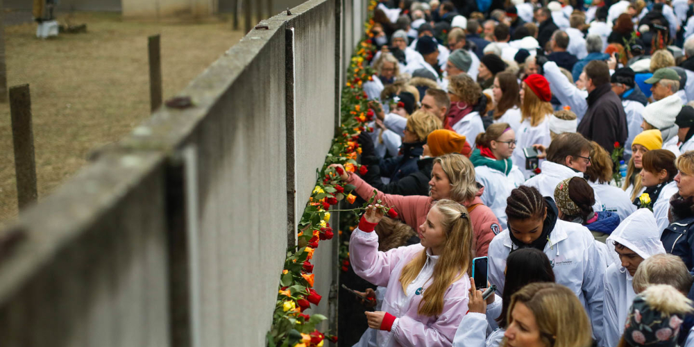 Na Bernauer Strasse, uma rua em Berlim, pessoas colocam flores no que sobrou do Muro de Berlim durante uma comemoração de sua queda em 2019 (© Markus Schreiber/AP)