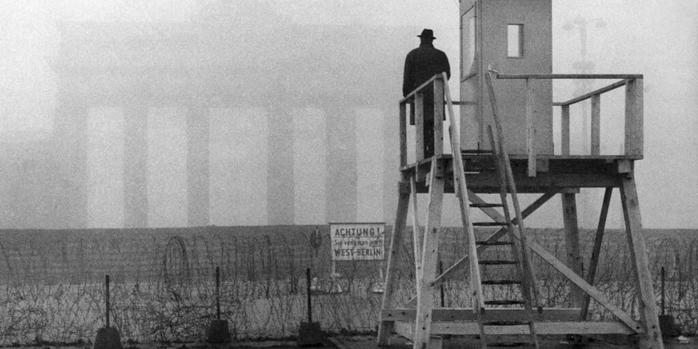 Nesta imagem de 25 de novembro de 1961, o Portão de Brandemburgo está envolto em neblina enquanto um homem olha de uma torre de vigilância sobre o muro que divide Berlim (© Heinrich Sanden Sr./AP)